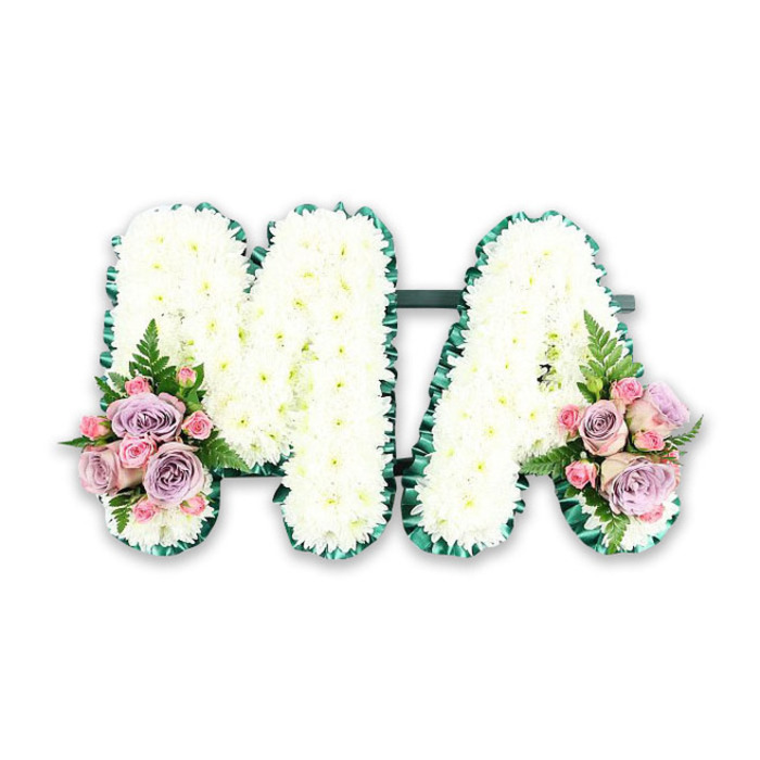 Displayed against a clean white background, this floral design shows a bespoke funeral letter tribute spelling out MA, likely chosen to honour a mother, Mama, or a loved one with those initials. The letters are bold yet softened by their floral covering, each one meticulously coated in pristine white chrysanthemums. These small, rounded blooms are so closely packed that they form a dense, cushiony surface, the petals overlapping like tiny feathers. The subtle variations in petal size and shape add texture and dimension, catching the light in a way that makes the arrangement feel gentle and alive, much like the calm residential streets and gardens around Norbiton on a still morning. A deep green satin ribbon runs around the outside of each letter, forming a crisp border. The ribbon is carefully pleated and ruffled, following every angle and corner of the M and the A. This darker frame provides a pleasing contrast to the white flowers while echoing the natural greens of local parks and tree-lined avenues, giving the piece both clarity and elegance. At the base of the left leg of the M and the right leg of the A, matching accent sprays have been added. These are composed of soft lilac roses, delicate pink roses, and smaller pink spray roses, arranged close together so that their velvety petals create small islands of colour. Fine fern fronds extend from these clusters, adding light, airy greenery and softening the transitions between the letters and the surrounding space. The tribute feels heartfelt and composed, the kind of personalised arrangement a family in Norbiton might request when they wish to express love, gratitude, and remembrance in a way that words alone cannot fully capture.
