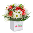 Effortlessly joyful and brimming with colour, this bouquet is a vivid emblem of Norbiton's heartfelt approach to floristry. Resting upright in a gleaming white square gift bag, plush coral and peach carnations unfold in layers of ruffled softness, instantly evoking the fresh promise of spring across Norbiton's leafy avenues. Lively white daisies, each with a golden-green eye, lend a playful, sunny uplift, while airy clusters of baby's breath float gracefully between the blooms, offering a gauzy sense of light and movement. Hidden among this bounty, a few closed purple-tinged buds add a note of mystery and anticipation. Abundant, glossy green foliage provides a lush, supportive frame, hugging the arrangement in a way that's both nurturing and striking. The presence of the sturdy ribbon-handled white gift bag suggests effortless gifting or timely delivery across Norbiton, reinforcing the arrangement's role as a thoughtful gesture for birthdays, new beginnings, or everyday celebrations. Bathed in luminous, even light and set against a flawless white backdrop, every detail shines-each stem, bloom, and leaf arranged with expert precision and a sense of genuine warmth. This bouquet feels like a bright wish made tangible, ready to lift spirits and brighten homes throughout the local community.